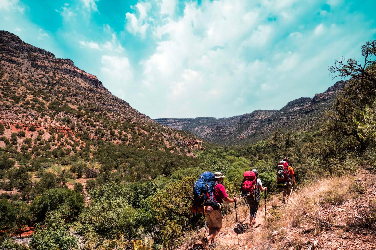 Hikers with backpacks descending a shaded Sedona canyon trail